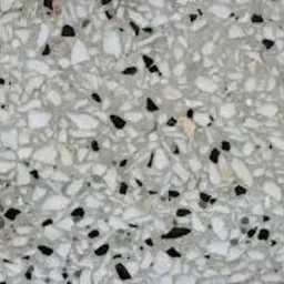 Powierzchnia z konglomeratu z wyraźnymi, nieregularnymi fragmentami białego i czarnego kamienia zatopionymi w szarej matrycy.