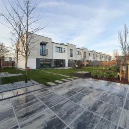 Nowoczesny ogród szeregowy z równo ułożoną kostką brukową, świeżo posianą trawą i minimalistycznym ogrodzeniem z siatki.