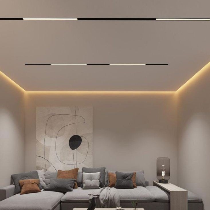 Nowoczesny salon z szarą sofą, abstrakcyjnym obrazem i liniowym oświetleniem sufitowym LED z dodatkowym oświetleniem ambientowym wzdłuż krawędzi sufitu.