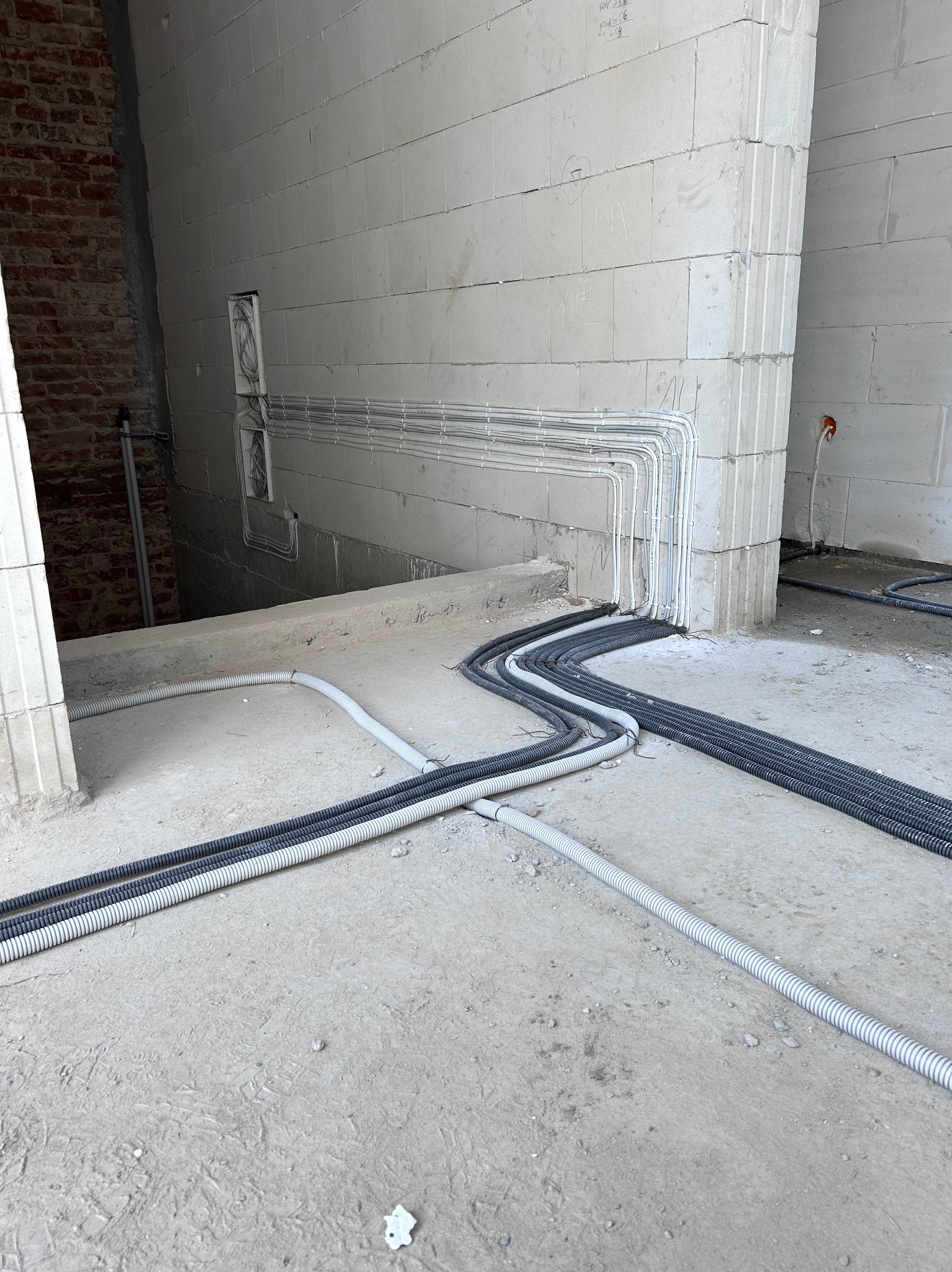 Wnętrze w trakcie prac: szare i białe peszle ułożone na surowym betonie, prowadzące do białych ścian z betonu komórkowego, gdzie widoczne są puszki instalacyjne.