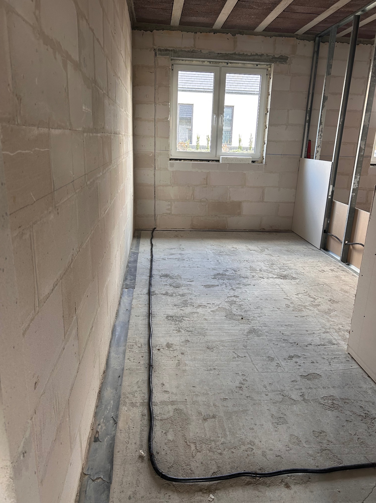 Surowy stan wnętrza: ściany z betonu komórkowego, okno, instalacja elektryczna w peszlu przy podłodze, profile pod płyty gipsowe. Wnętrze w trakcie remontu.