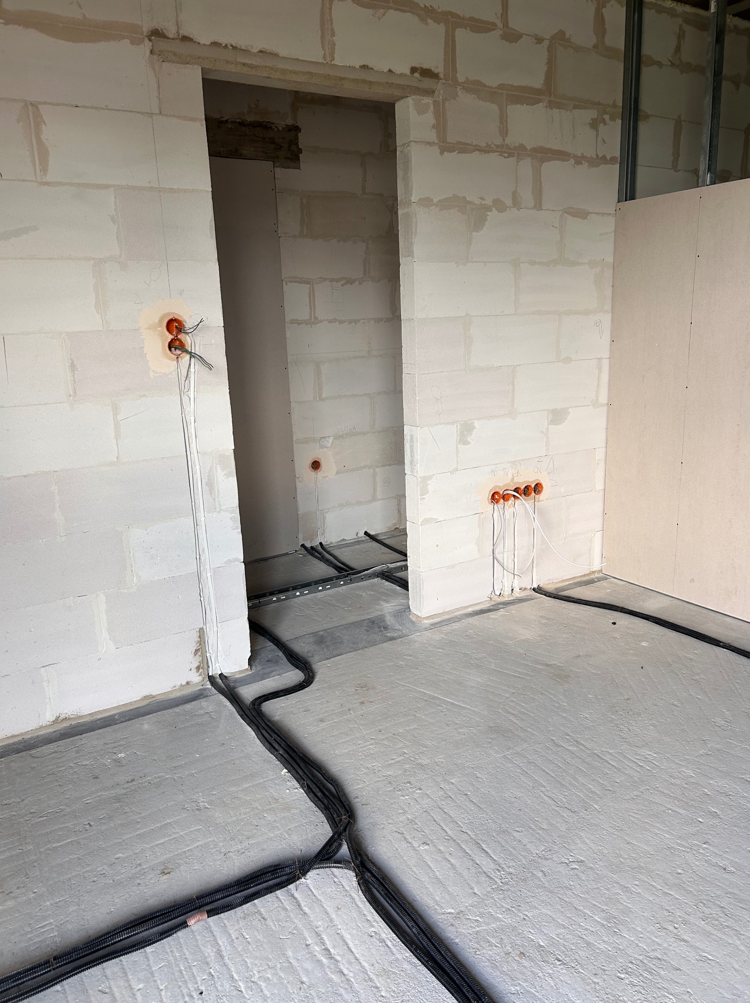 Surowy stan wnętrza: widoczne przewody elektryczne w ścianach z betonu komórkowego i rury instalacyjne na podłodze, przygotowane do dalszych prac wykończeniowych.