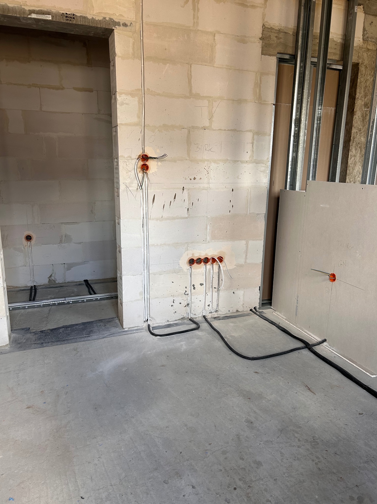 Surowy stan: instalacja elektryczna w ścianach z betonu komórkowego i rurki pod podłogą, widoczne profile do płyt gipsowych. Wnętrze w trakcie prac wykończeniowych.