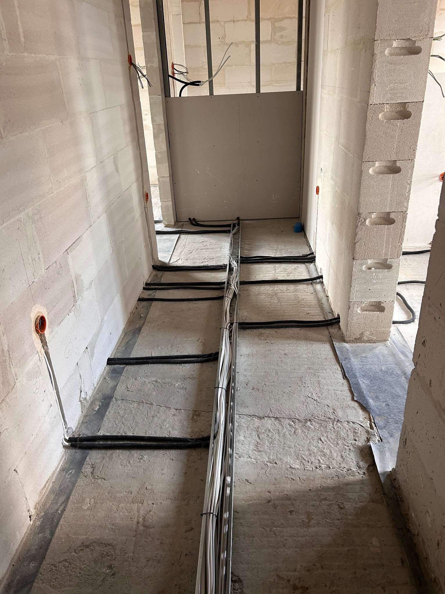 Wnętrze w trakcie prac: widoczne kable w peszlach ułożone na podłodze, ściany z betonu komórkowego z puszkami elektrycznymi, metalowy stelaż i płyta G-K.
