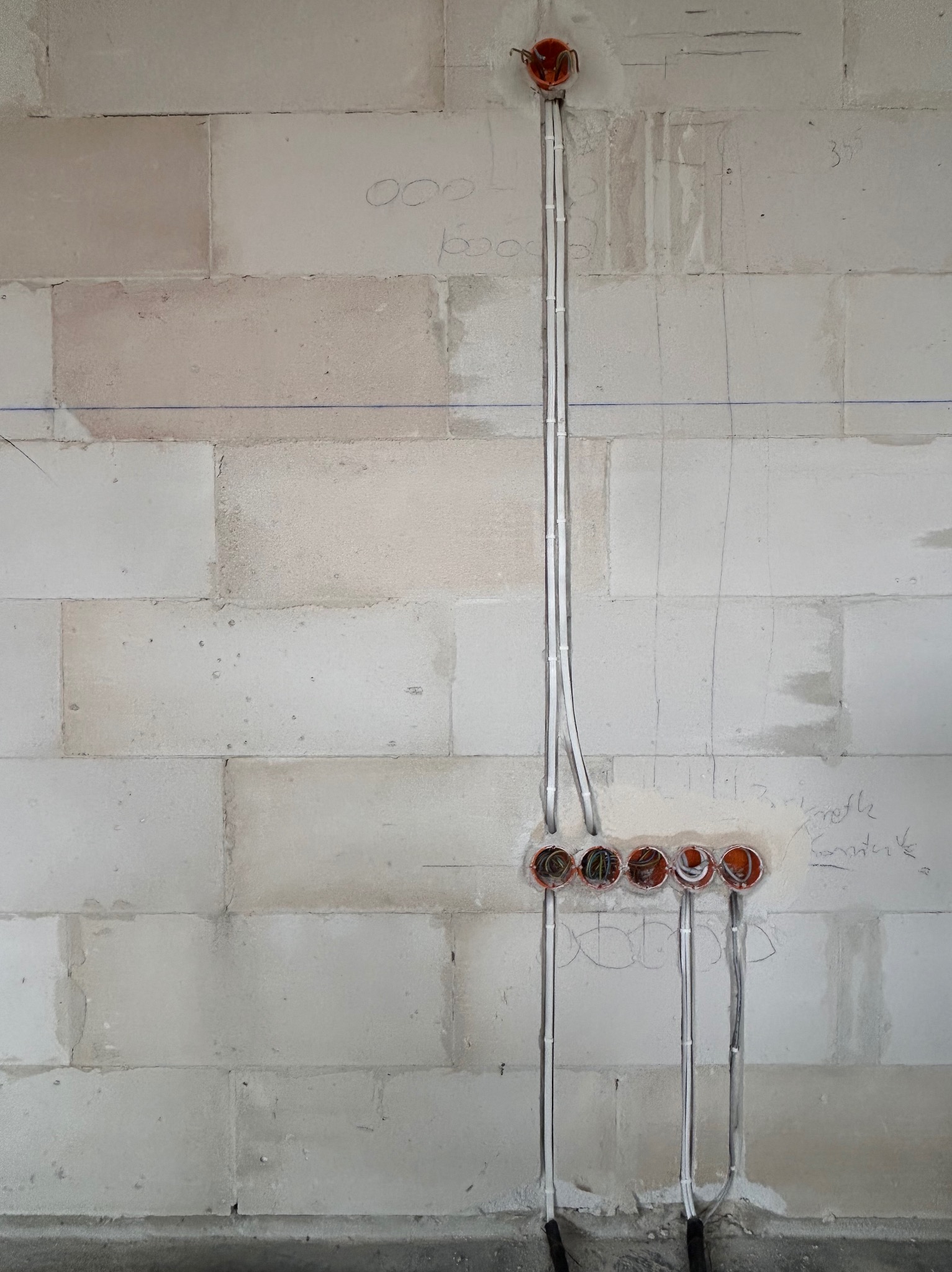 Instalacja przewodów elektrycznych w ścianie z betonu komórkowego, widoczne puszki instalacyjne. Na ścianie widoczne pomocnicze oznaczenia ołówkiem.