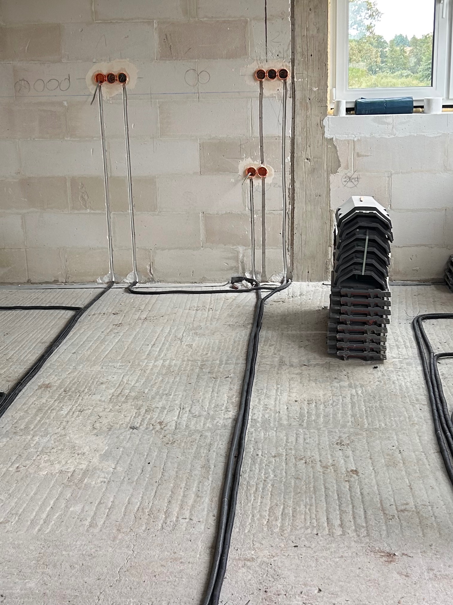 Surowy stan: kable elektryczne w podłodze, puszki w ścianie z betonu komórkowego, przygotowane do dalszych prac wykończeniowych. Widok na okno w tle.