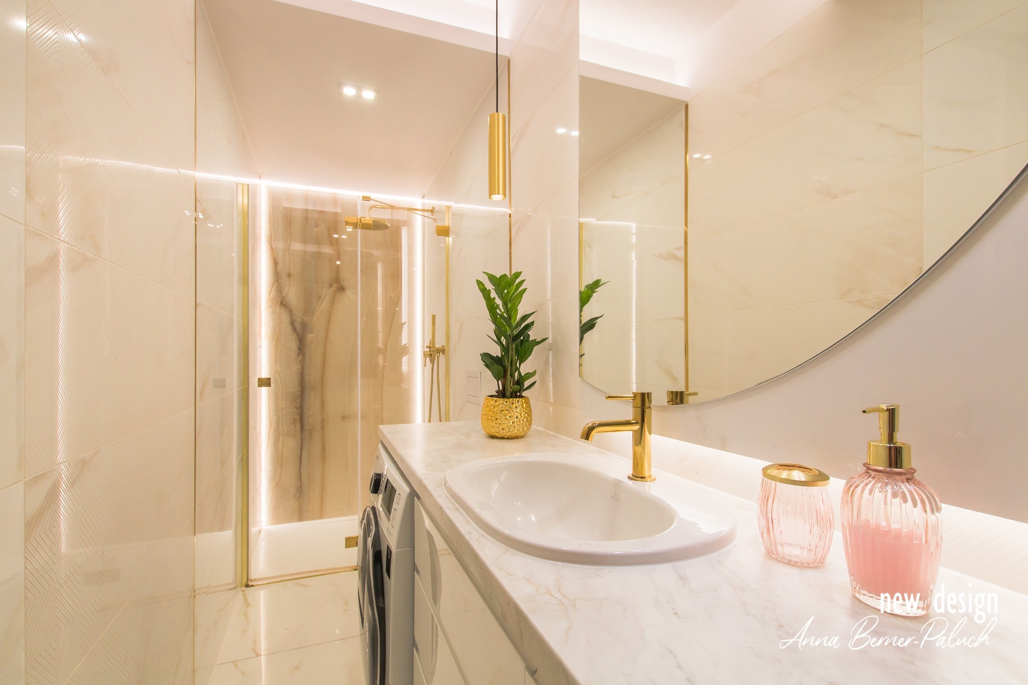 Ekskluzywna łazienka z onyksową kabiną prysznicową, złotą armaturą i rośliną w ozdobnej, złotej doniczce. Umywalka wpuszczona w marmurowy blat, obok dozownik mydła w odcieniach różu. Widoczny...