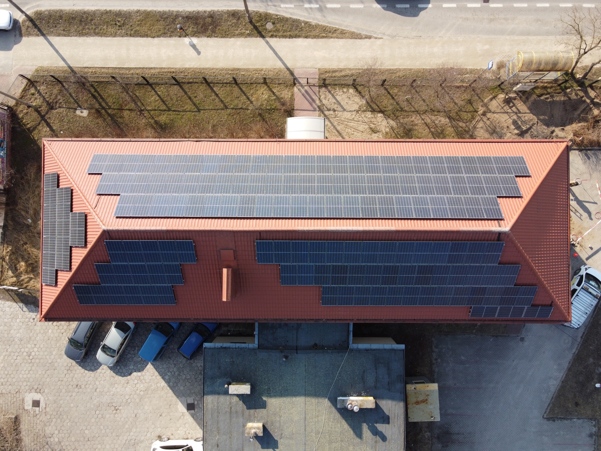 Widok z góry na budynek z panelami słonecznymi na dachu w Tomaszowie Mazowieckim, obok zaparkowane samochody.