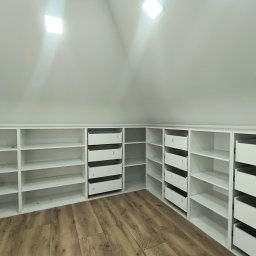 Mk meble Mariusz koczynasz - Biała szafa wnękowa z szufladami i półkami, dopasowana do skosu poddasza. Jasne drewniane panele podłogowe, oświetlenie sufitowe.