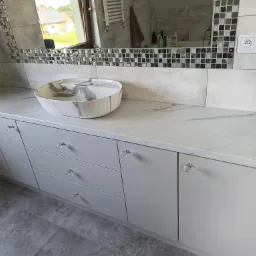 Łazienkowa szafka z blatem imitującym marmur i umywalką nablatową. Kryształowe gałki, lustro z mozaiką. Nowoczesny design.