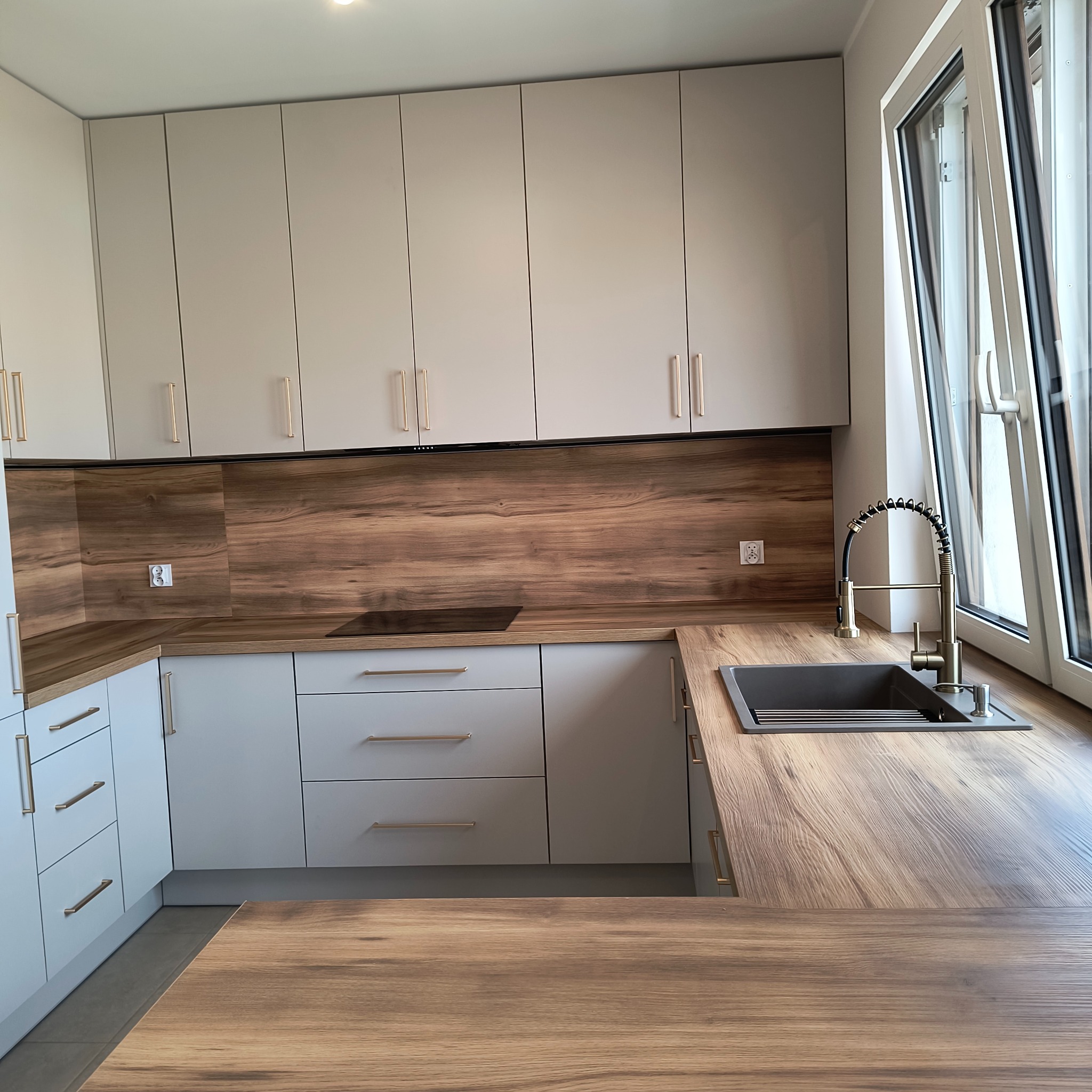 Jasna kuchnia na wymiar z drewnianym blatem i złotymi uchwytami, nowoczesny design, widok na okno, minimalistyczny styl.