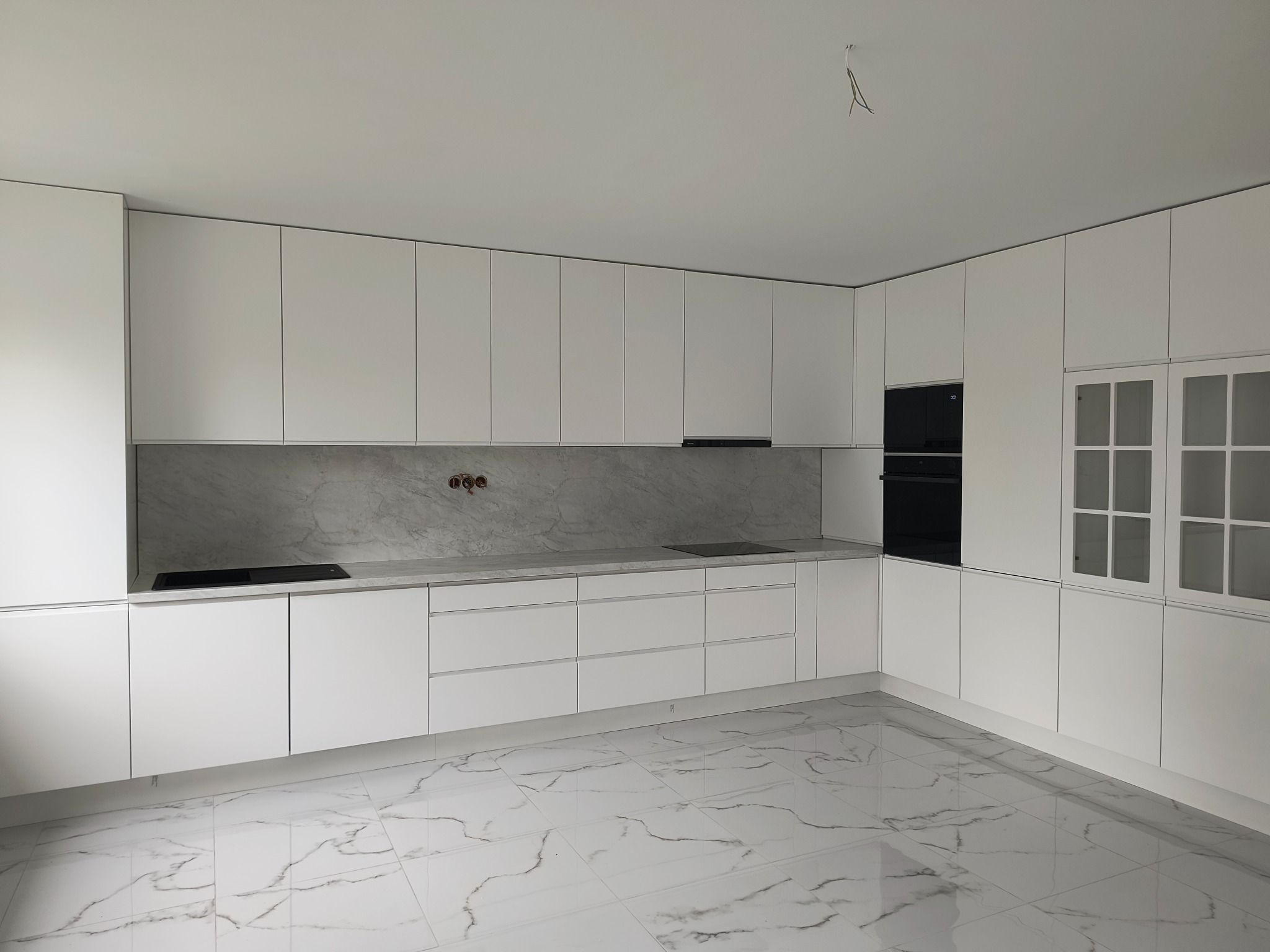 Nowoczesna, minimalistyczna kuchnia w bieli z marmurowym blatem i podłogą. Widok na zabudowę kuchenną z frontami bez uchwytów i sprzętem AGD.