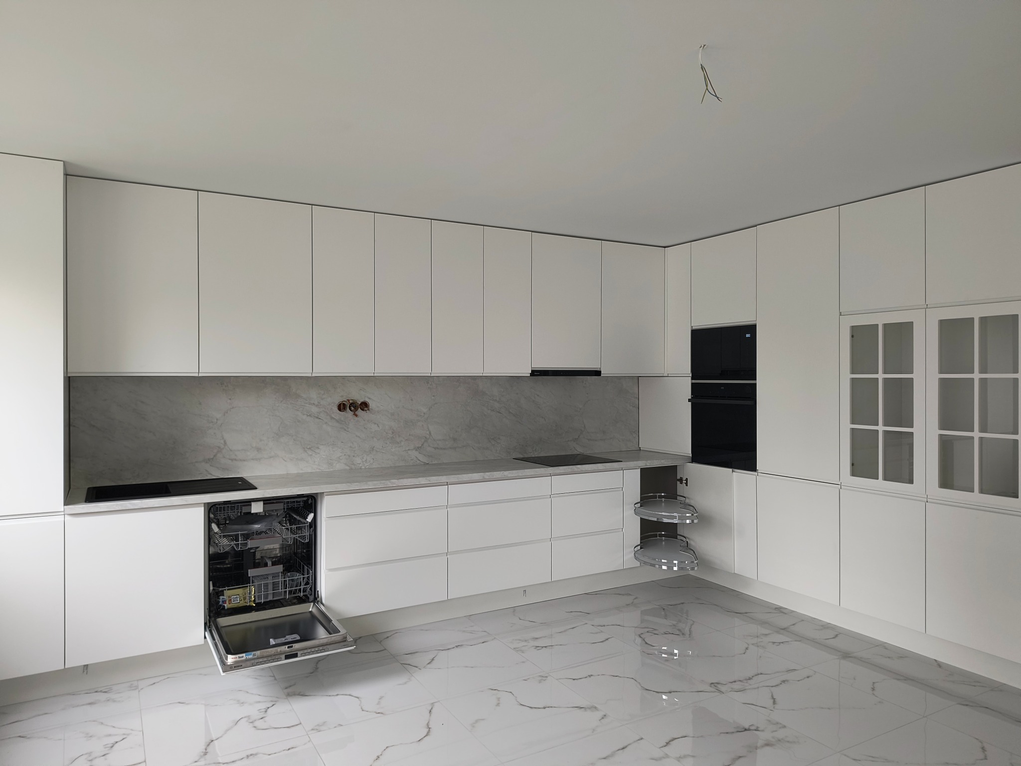 Nowoczesna, minimalistyczna kuchnia z białymi frontami, marmurowym blatem i otwartą zmywarką. Widoczne elementy wyposażenia i wykończenia.