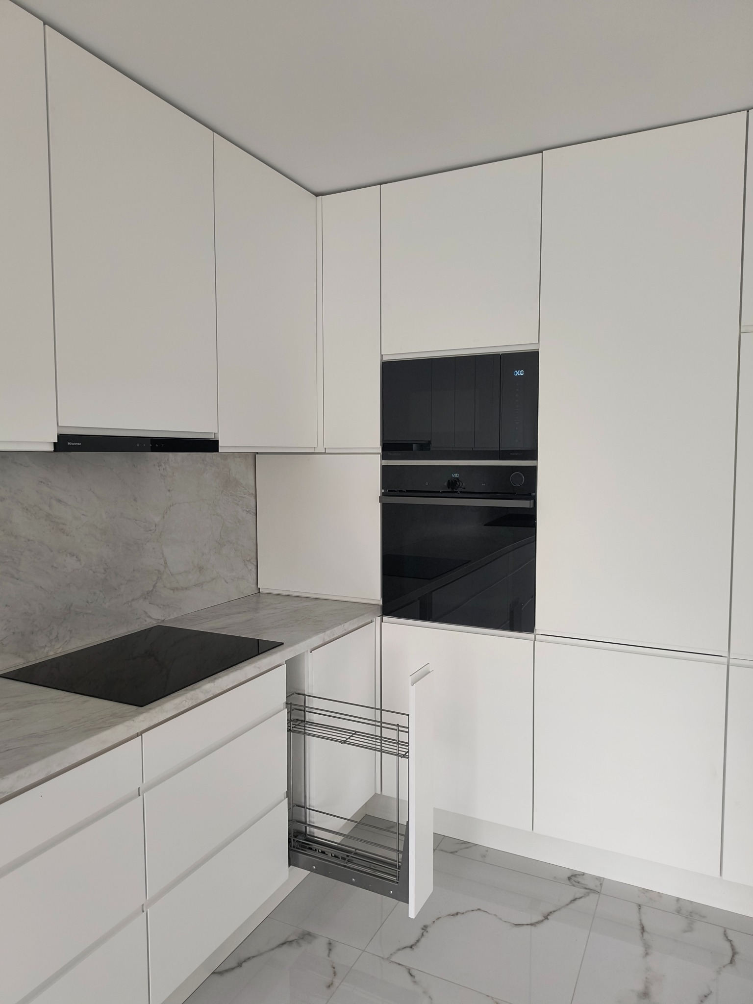Minimalistyczna kuchnia w bieli z marmurowym blatem i wysuwanym cargo, nowoczesny design z piekarnikiem i płytą indukcyjną. Fronty bez uchwytów, błyszcząca podłoga.