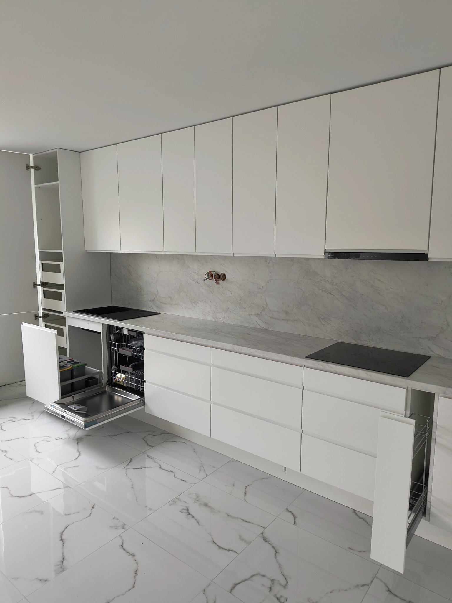 Biała, minimalistyczna kuchnia z marmurowym blatem i otwartą zmywarką. Widoczne szuflady na prowadnicach i szafki wiszące.