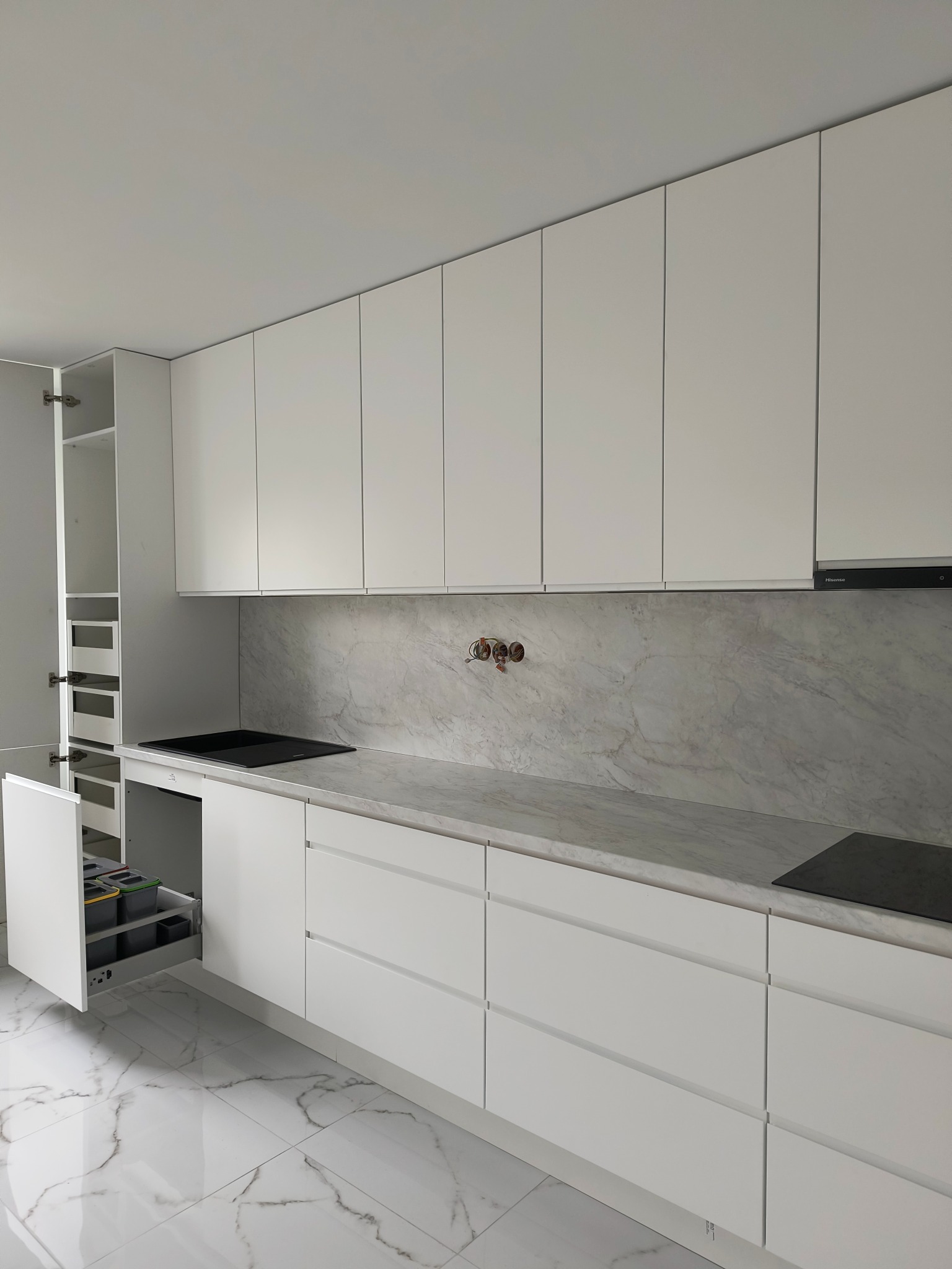 Biała kuchnia z marmurowym blatem i otwartą szafką cargo. Widoczne sortowniki na śmieci. Minimalistyczny design, nowoczesne wykończenie, błyszcząca podłoga.