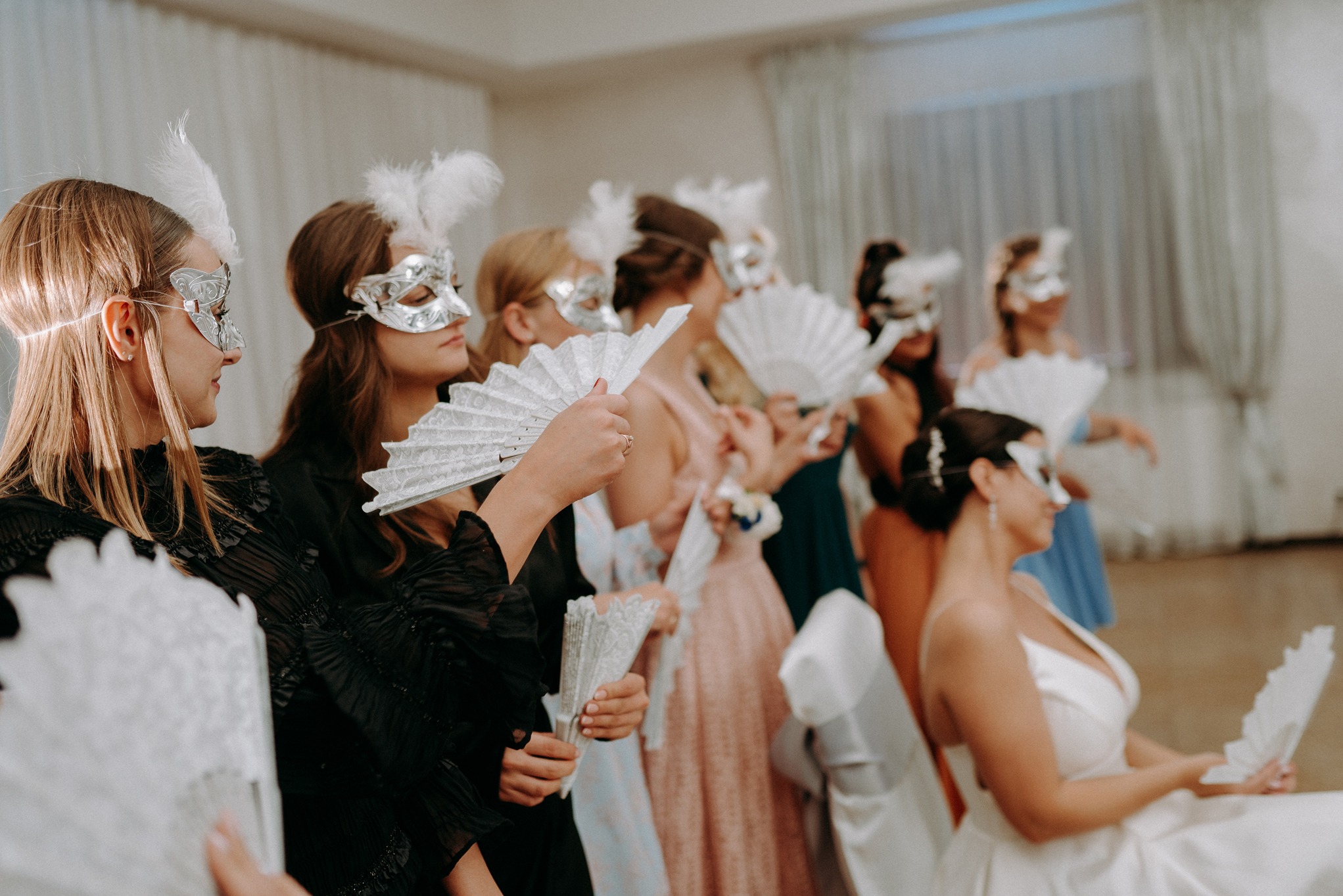 Grupa kobiet w maskach karnawałowych i z wachlarzami w Suwałkach, przygotowująca się do występu na balu maskowym.