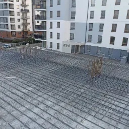 Siatka zbrojeniowa przygotowana do zalania betonem na budowie w Bydgoszczy, widok z g&oacute;ry na tle nowego bloku mieszkalnego.