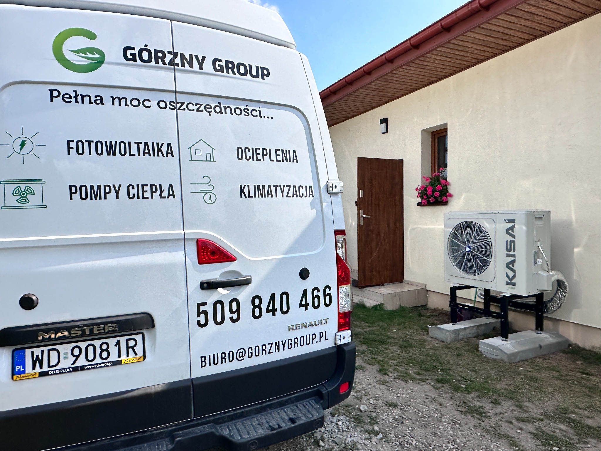 Biały samochód dostawczy firmy Górzny Group z reklamą usług: fotowoltaika, pompy ciepła, ocieplenia i klimatyzacja, zaparkowany obok budynku z zamontowaną jednostką zewnętrzną klimatyzacji Kaisai.