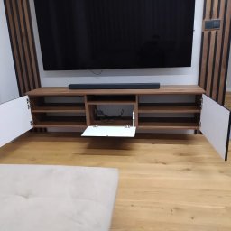 Max furniture - Drewniana szafka RTV z otwartymi białymi frontami, widoczne okablowanie, soundbar na blacie, tło stanowią panele dekoracyjne na ścianie.