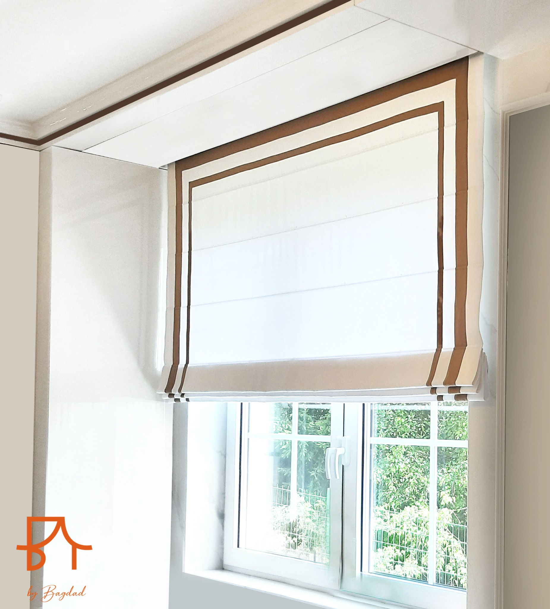 Elegancka, biała roleta rzymska z brązowym obramowaniem, zamontowana w oknie z widokiem na zieleń, częściowo zwinięta, z widocznym logo firmy w lewym dolnym rogu.