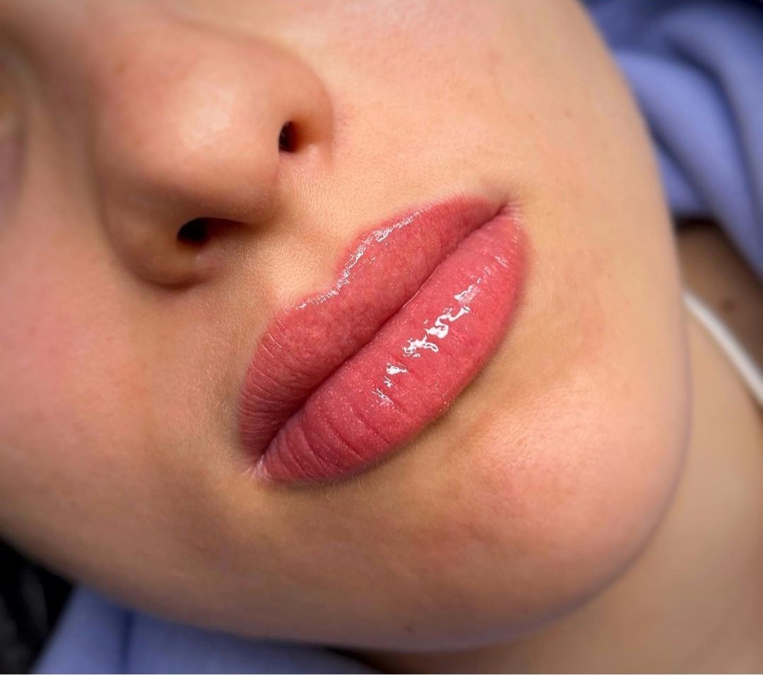 Zbliżenie na usta po zabiegu makijażu permanentnego, widoczne delikatne zaczerwienienie wokół ust i błyszczący efekt na nich.