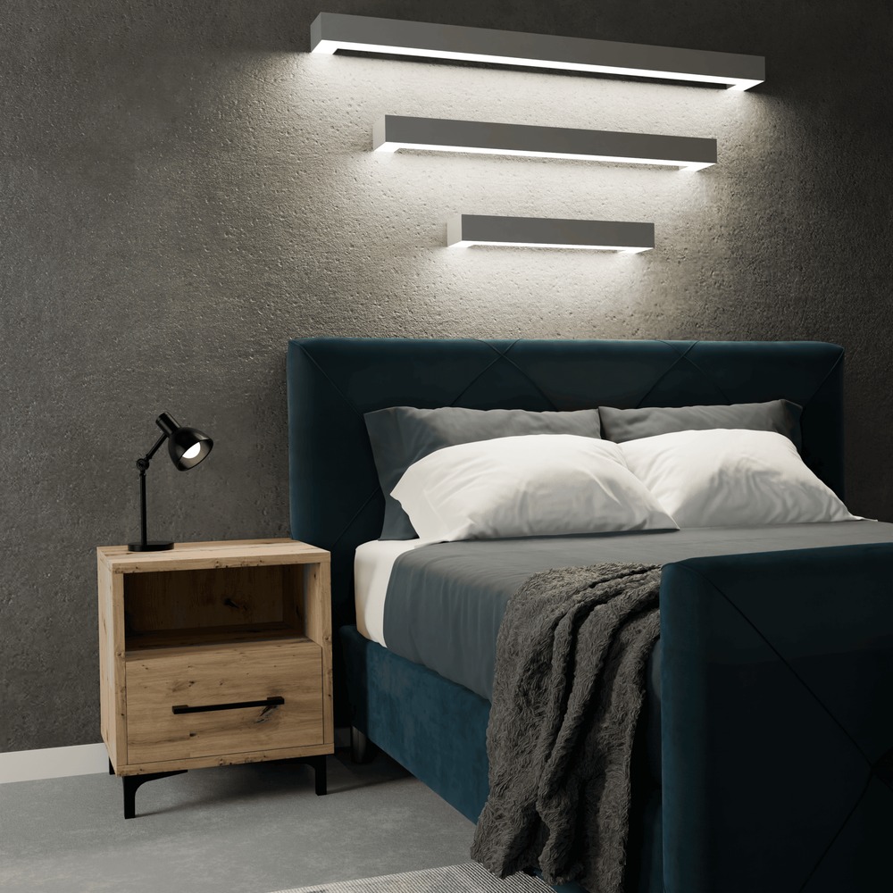 Szafka nocna Dąb Artisan z szufladą i oświetleniem LED, ustawiona obok łóżka z welurowym zagłówkiem w odcieniach granatu i szarości, na tle betonowej ściany z trzema podłużnymi lampami.