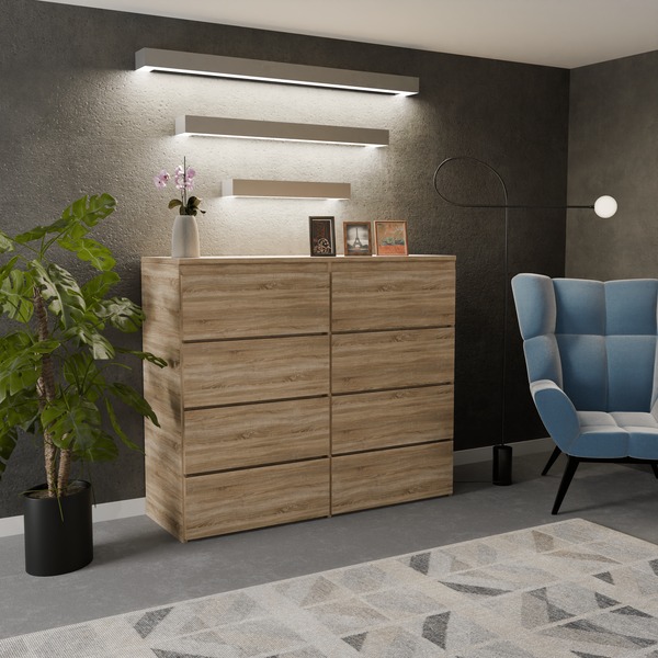 Komoda z sześcioma szufladami w kolorze dębu sonoma, bez uchwytów, ustawiona w pokoju z niebieskim fotelem i rośliną doniczkową, oświetlona trzema podłużnymi lampami ściennymi.