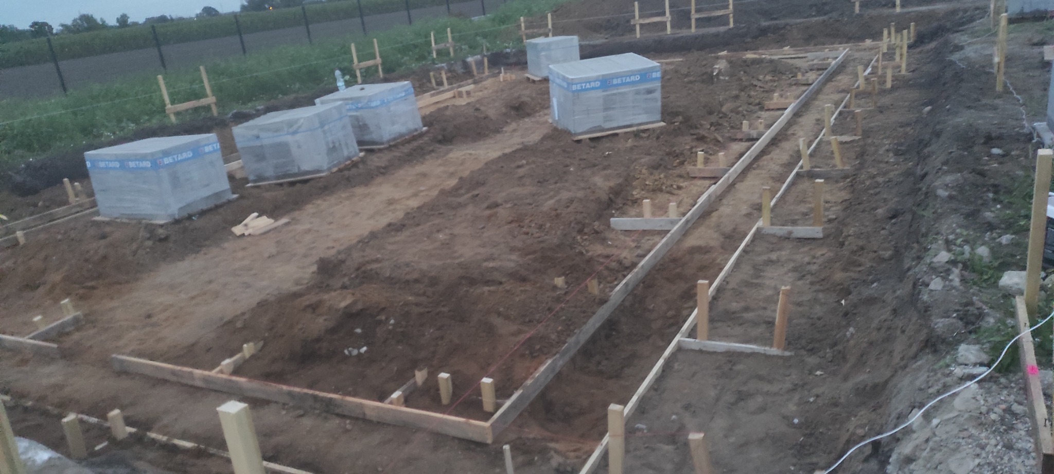 Przygotowanie fundamentów pod budowę domu: drewniane szalunki, wykopane rowy i ułożone bloczki betonowe Betard na placu budowy.