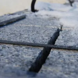 Cięta kostka brukowa z fakturą, z widocznymi fugami wypełnionymi materiałem, częściowo pokryta śniegiem.