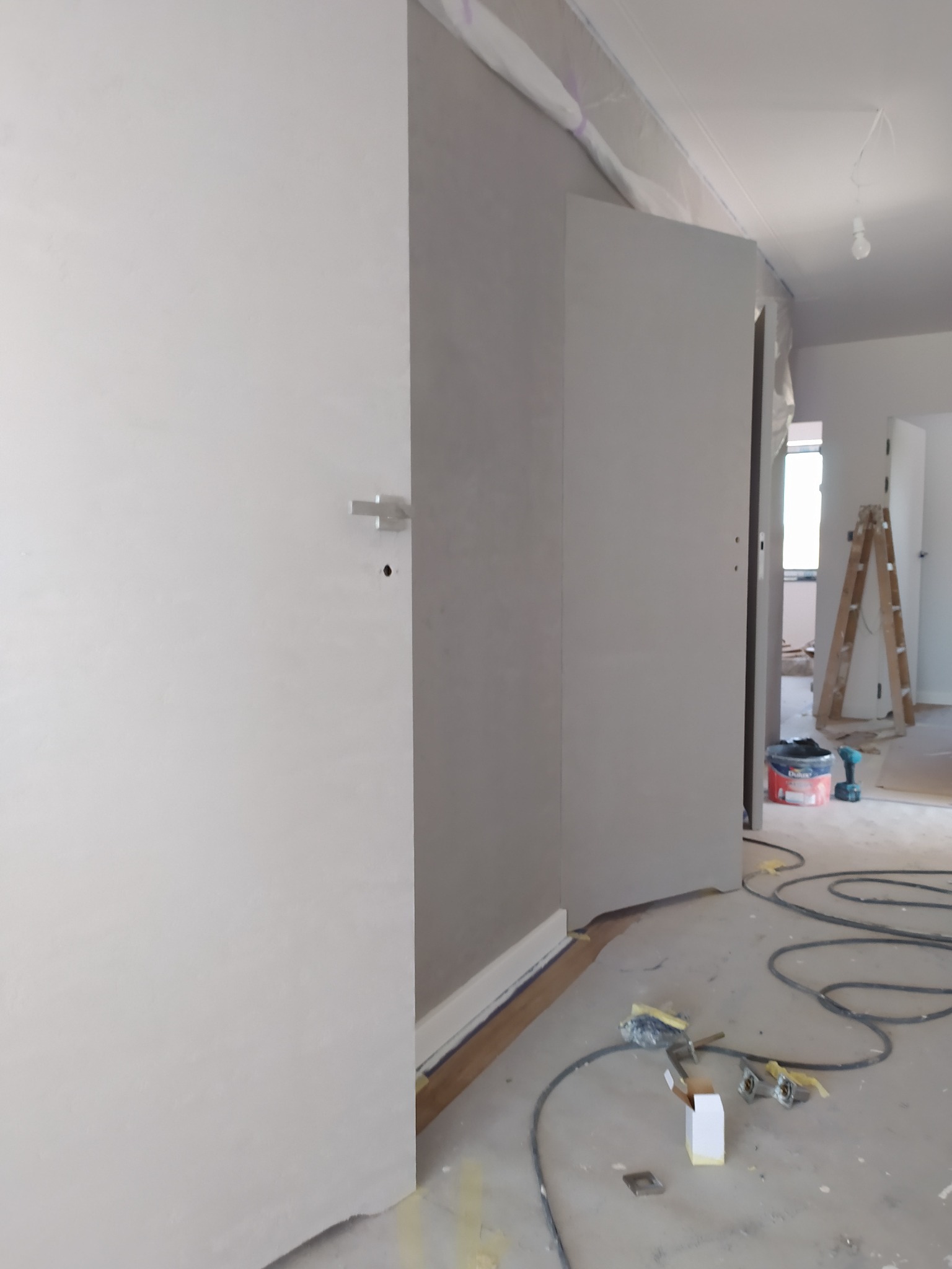 Wnętrze w trakcie wykończenia: ściany po nałożeniu gładzi, widoczne narzędzia, szpachle, drabina w tle, zabezpieczona folią listwa sufitowa.