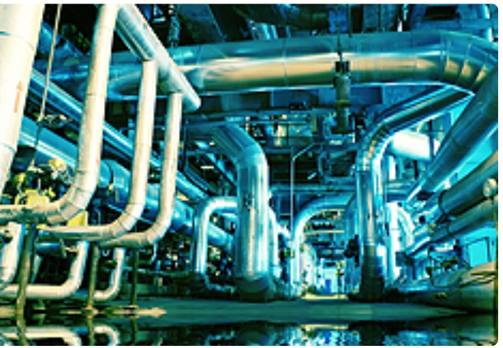 Złożona instalacja przemysłowa z rurami o różnej średnicy i kształcie, wykonana z metalu, oświetlona niebieskim światłem, tworząca labirynt w przestrzeni przemysłowej.