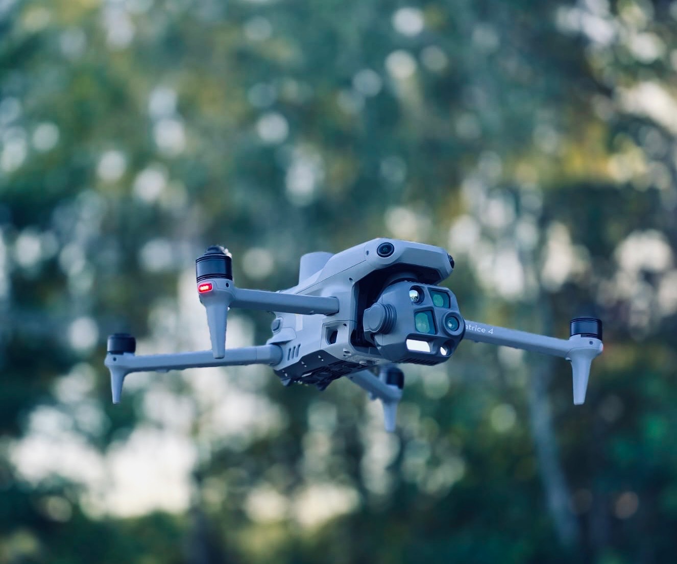 Szary dron Matrice 4 w locie, z widoczną kamerą i czujnikami, na tle rozmytej zieleni. Usługi detektywistyczne we Wrocławiu z wykorzystaniem drona.