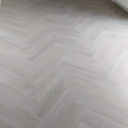 Jasna, nowa podłoga z paneli ułożonych we wzór jodełki francuskiej w rogu pokoju z białymi ścianami i grzejnikiem.