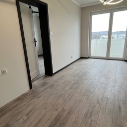 Łukasz, kafle, remonty, wykonczenia. - Jasne panele podłogowe w nowym wnętrzu z nowoczesnym oświetleniem. Widoczne drzwi z czarną ramą i duże okno balkonowe. Minimalistyczny design.