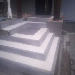 Wykończone schody wejściowe z jasnych płytek, z elementami dekoracyjnymi i kolumnami z obłożonego kamienia, widok z góry na fragment tarasu.