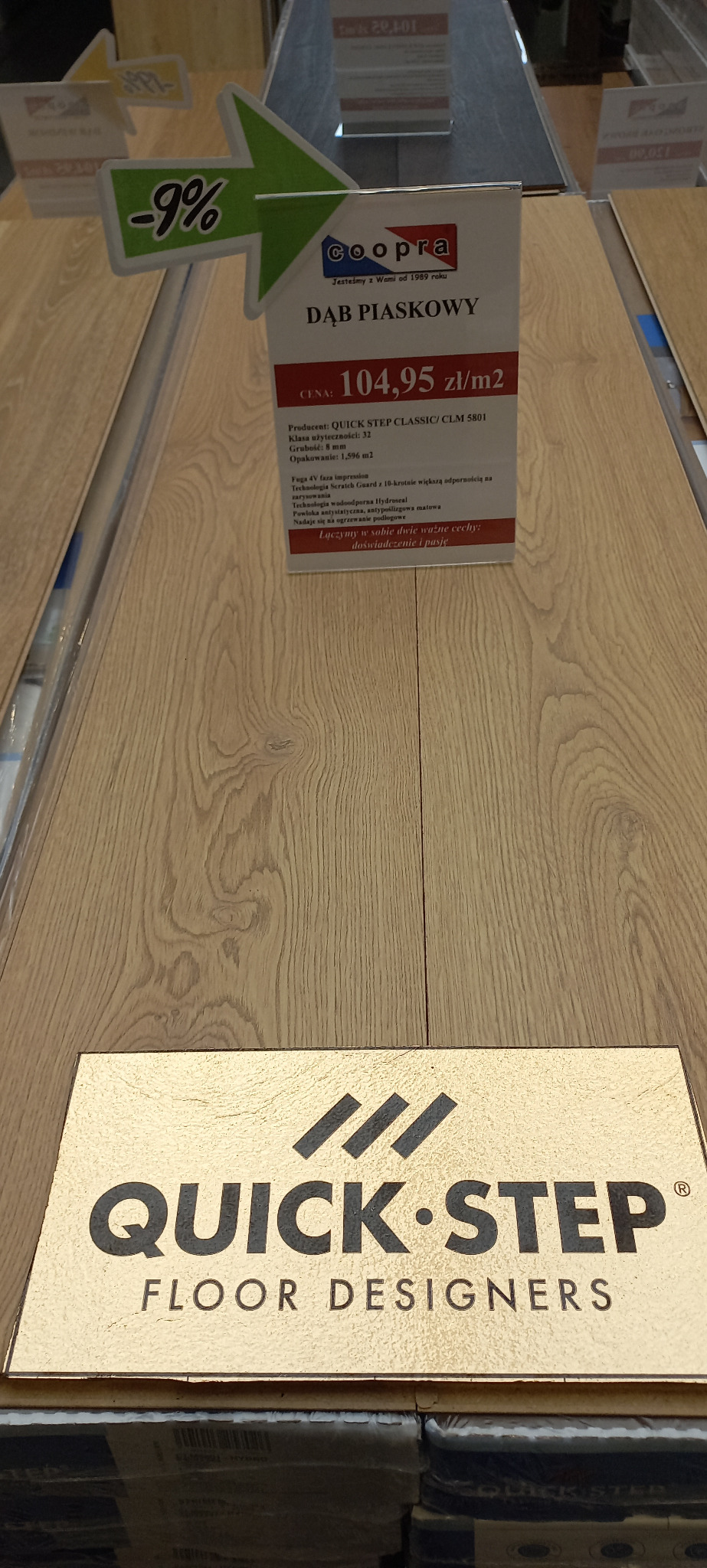 Panele podłogowe Quick-Step Dąb Piaskowy, prezentacja w sklepie z ceną i informacjami o produkcie, widoczne opakowania paneli.