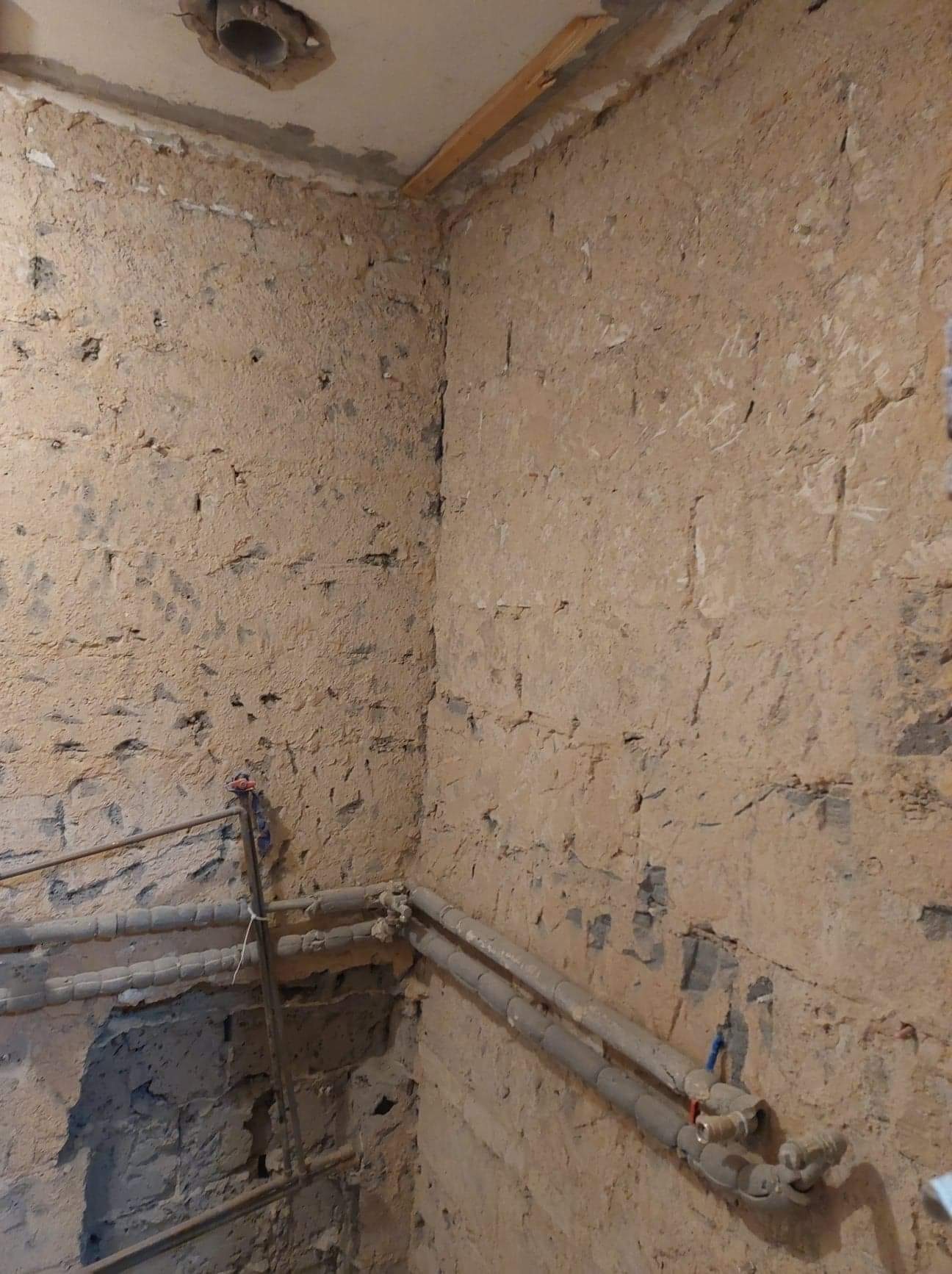 Surowe ściany w rogu pomieszczenia z widocznymi rurami instalacji wodnej, przygotowane do dalszych prac wykończeniowych.