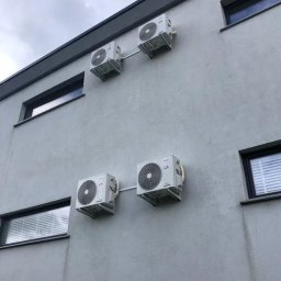 SERKOWSKI Chłodnictwo i Klimatyzacja - Cztery klimatyzatory zamontowane na szarej ścianie budynku z oknami, widok z dołu na pochmurne niebo.