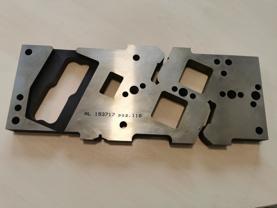 Precyzyjnie obrobiony metalowy element z wyfrezowanymi otworami i wgłębieniami, oznaczony numerem seryjnym AL 193717 poz. 118, leżący na jasnym tle.