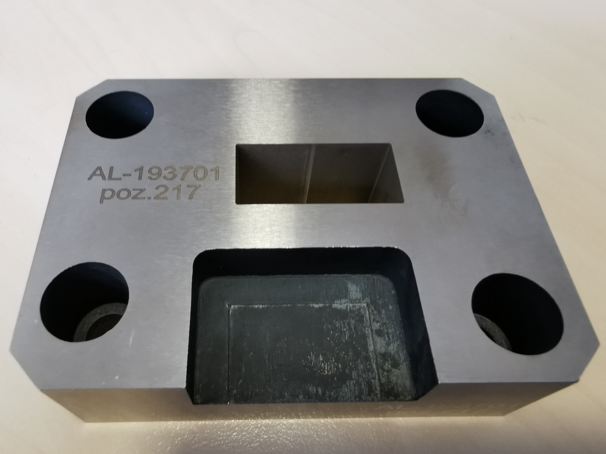 Szlifowany, metalowy element z wyfrezowanymi otworami i wgłębieniami, oznaczony numerem AL-193701 poz.217, leżący na jasnej powierzchni.