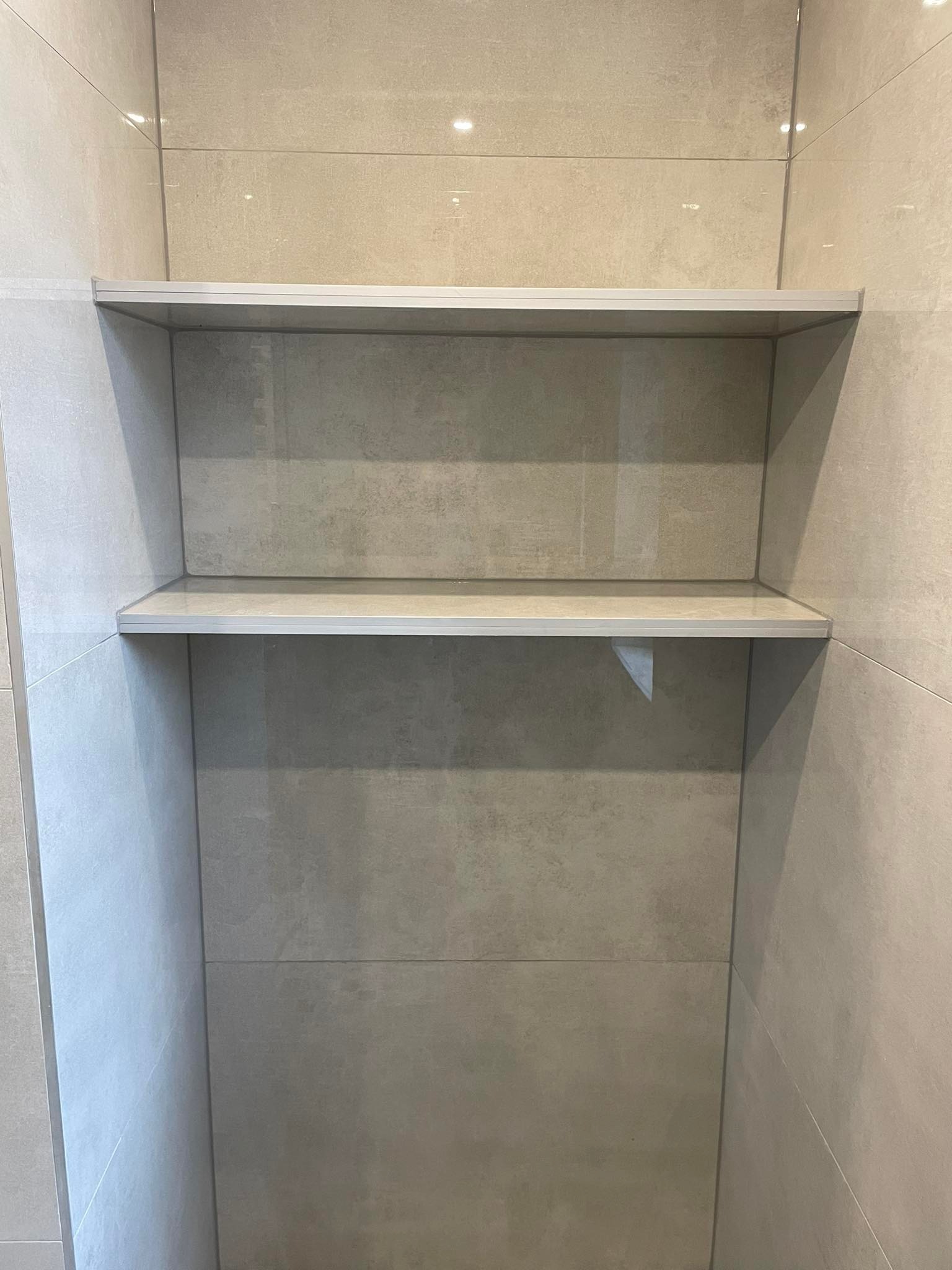 Półki wnękowe wyłożone szarymi płytkami imitującymi kamień, z aluminiowymi krawędziami, w nowoczesnej łazience.