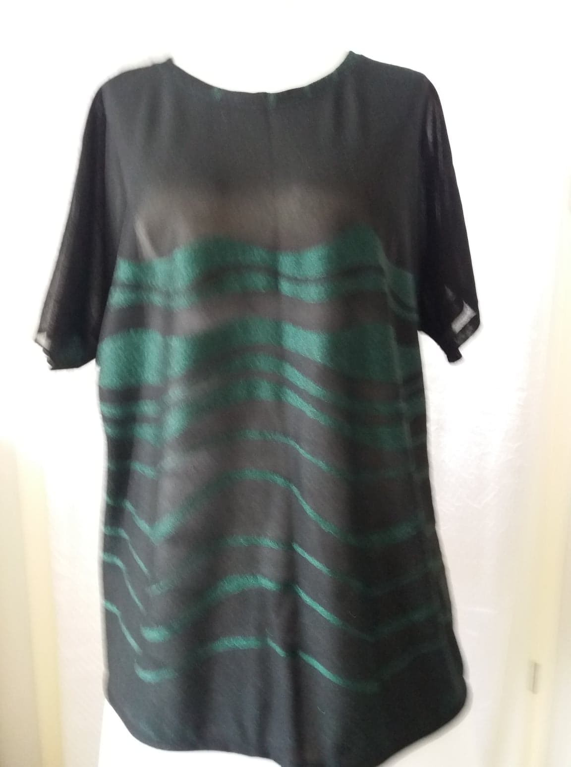 Czarna, półprzezroczysta bluzka z krótkim rękawem i zielonymi, falistymi paskami, widoczna na białym tle.