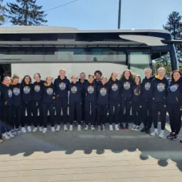 Grupa młodych sportowców w granatowych bluzach z kapturem i logo drużyny GTK Gdynia, stojących przed autokarem.