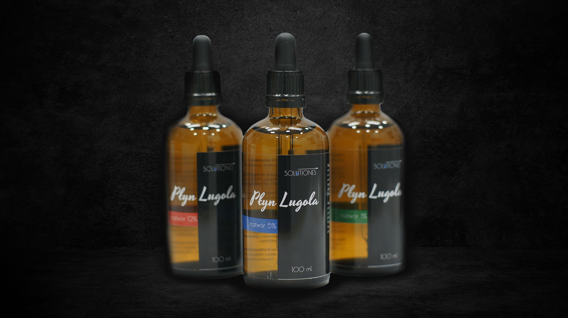 Trzy butelki z brązowego szkła z roztworem Lugola o różnym stężeniu (12%, 5%, 19%) na czarnym teksturowanym tle, prezentacja produktu.