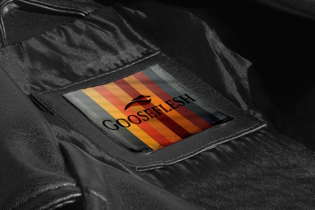Wnętrze czarnej skórzanej kurtki z wszytą metką z logo 'GOOSEFLESH' na tle kolorowych pionowych pasków.