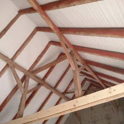 Konstrukcja drewniana dachu z widoczną białą membraną dachową od wewnątrz, częściowo pomalowana na czerwono, widok od dołu.