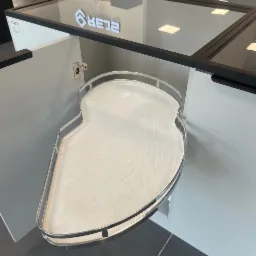 Wnętrze szafki narożnej z wysuwaną półką w kształcie nerki, chromowane obramowanie, białe fronty, nowoczesny design, oświetlenie LED na górze.