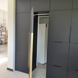 Mark Pol Meble - Nowoczesna, matowa, grafitowa szafa na wymiar z złotymi uchwytami, częściowo otwarta, ukazująca wnętrze z lodówką. Minimalistyczny design, jasna podłoga.