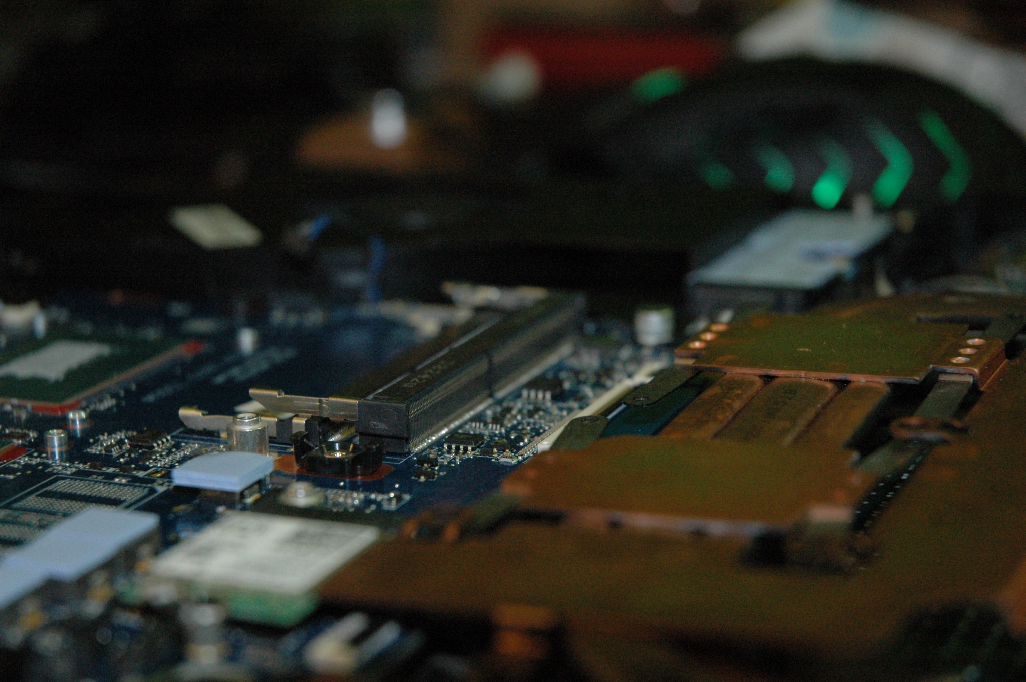 Zbliżenie na płytę główną laptopa z widocznymi elementami elektronicznymi, w tle rozmazana mysz z zielonymi akcentami.